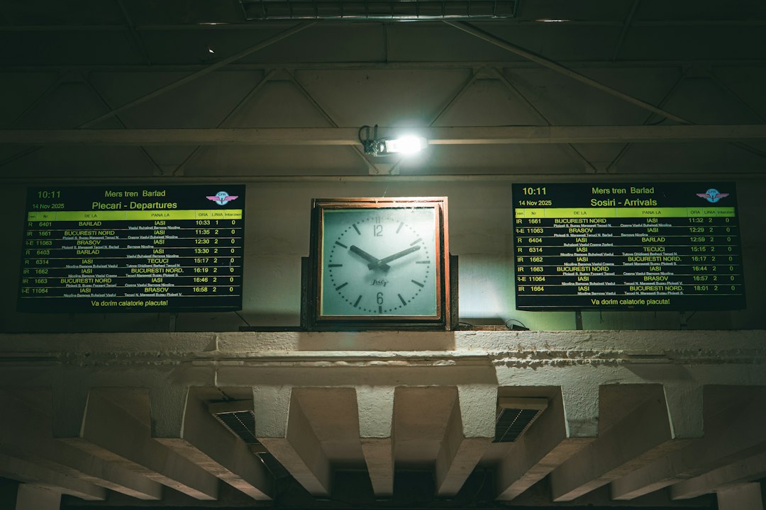 A square analog clock between two digital train departure and arrival boards